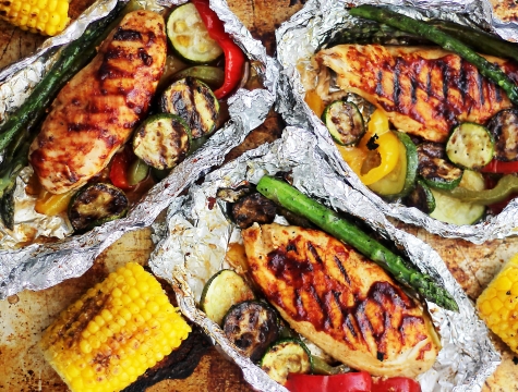 grilled chicken, asparagus, corn on the cob, zucchini and peppers sitting in aluminum foil packets