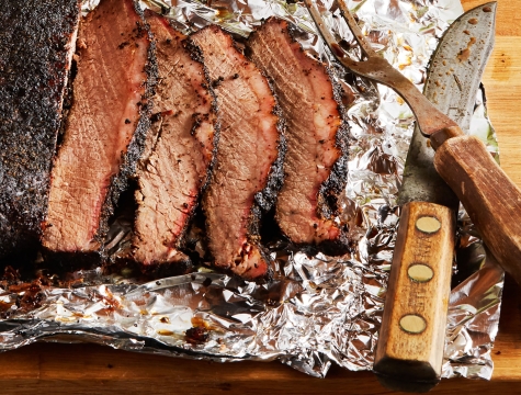Sliced brisket on a sheet of aluminum foil alongside a carving knife and fork