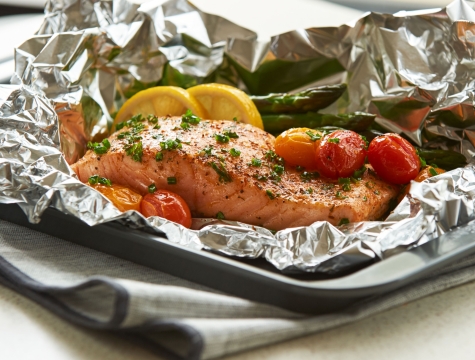 Salmon topped with lemons and tomatoes sitting on a sheet of non-stick aluminum foil