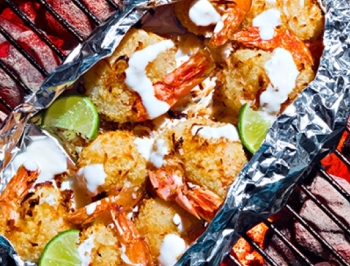 Coconut lime shrimp sitting in an aluminum foil grill pan on a charcoal grill