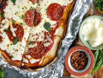 pepperoni pizza sitting on a sheet of aluminum foil alongside additional pizza toppings and seasonings