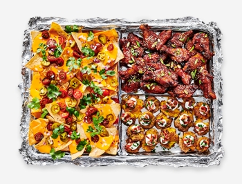 Nachos, wings and loaded potatoes on a foil lined baking sheet