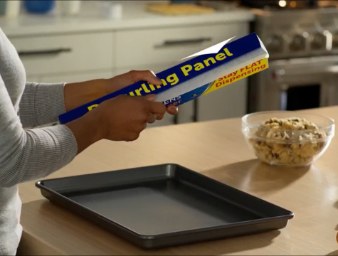 woman standing in a kitchen dispensing parchment paper for a pan