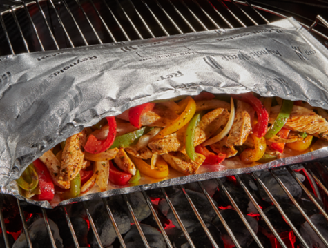 Open Reynolds Wrap Grill Bag Sitting on top of a hot grill with Chicken Fajitas in the bag