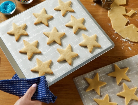 A person holding a parchment lined cookie sheet with star shaped sugar cookies