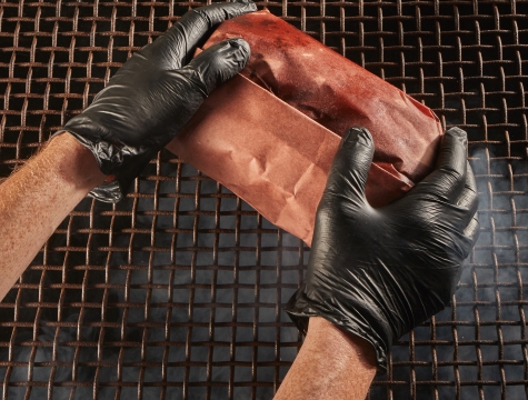 Person placing meat wrapped in Reynolds Kitchens Butcher Paper on a smoker