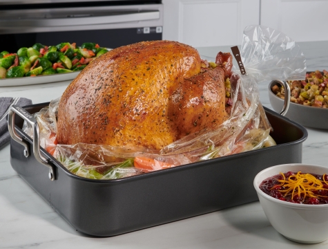 Roasted turkey sitting in an open oven bag in a roasting pan alongside various side dishes