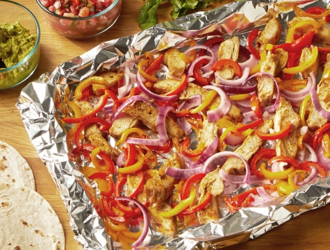 Chicken fajitas with sliced peppers and onions sitting on an aluminum foil lined baking sheet