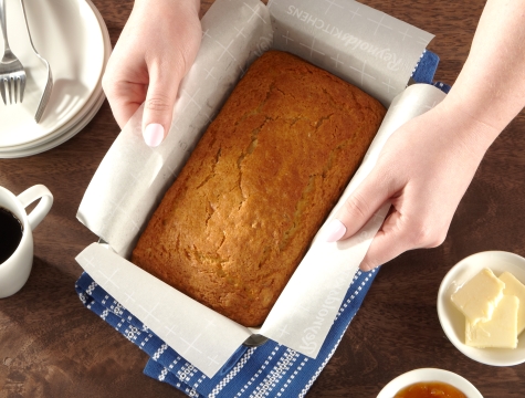 Person removing banana bread from a loaf pan with a parchment paper sling