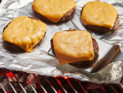 Cheeseburgers sitting on a sheet of aluminum foil on a charcoal grill