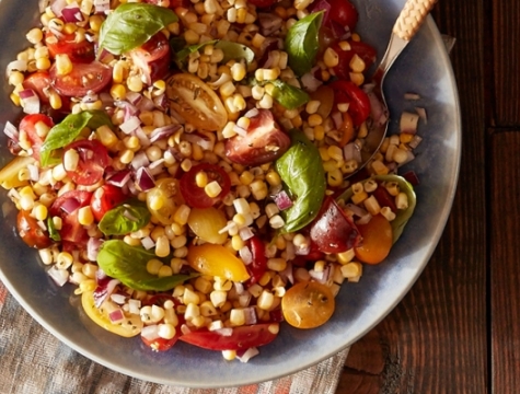 Grilled corn and heirloom tomato salad sitting in a bowl with a serving spoon on a table
