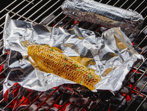 corn sitting on a sheet of aluminum foil on a charcoal grill