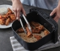 Person removing cooked chicken wings from an air fryer with a liner using tongs