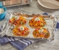 Cheese and chicken tostadas sitting on an aluminum foil lined baking sheet alongside a toaster oven
