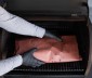 A person adding meat wrapper on pink paper to the grill