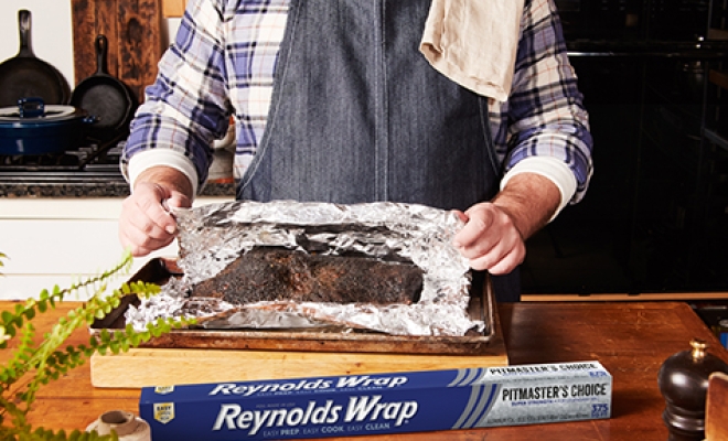 Person Unwrapping Cooked Brisket In Foil