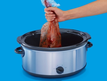 Person pulling a used slow cooker liner out of a slow cooker to be thrown away