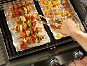 Person grilling food on a grill lined with aluminum foil