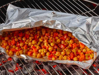Open Reynolds Grill Bag sitting on a hot charcoal grill with crunchy BBQ chickpeas inside