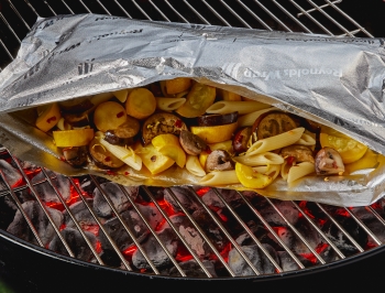 Open Reynolds Wrap Grill bag with lemony pasta with eggplant, mushroom and yellow squash inside sitting on a hot charcoal grill