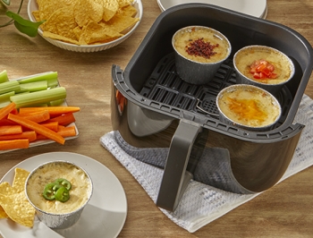 Reynolds Kitchens Air Fryer Cups filled with white queso dip sitting in an air fryer basket
