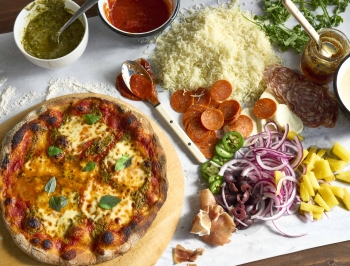 homemade pizza sitting on a cutting board on top of a sheet of Reynolds Kitchens Countertop Prep Paper topped with pizza toppings