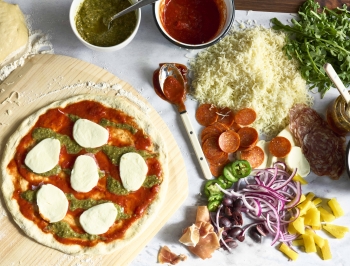 homemade pizza sitting on a cutting board on top of a sheet of Reynolds Kitchens Countertop Prep Paper topped with pizza toppings